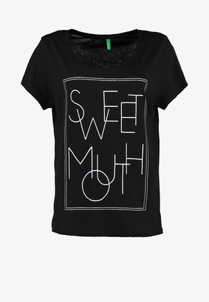 Mustat, hihattomat t-paidat, joissa on valkoinen geometrinen kuvitus, jossa lukee "SWEET". Yhdistettyinä vaalennetun harmaan farkkujen kanssa, joissa on käännetyt hihat, ja mustat nilkkurit.