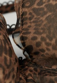 Bruin luipaardprint kant stof met een doorschijnende textuur, gedetailleerde stiksels en decoratieve zwarte accenten langs de randen.