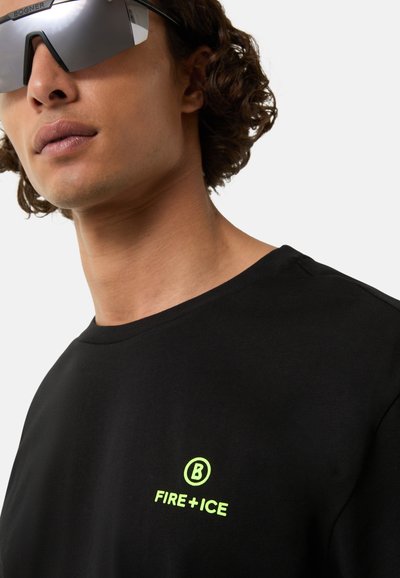 Sort t-shirt med rund hals, med et reflekterende gult logo "FIRE + ICE" på venstre bryst. Model iført spejlet solbriller.