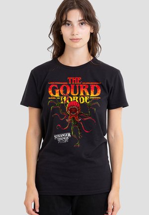 Young woman wearing black T-shirt with red and green monster graphic and text "The Gourd Horde" and "Stranger Things Tales from the Upside Down."
