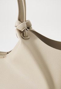 Beige skinnveske med tekstur, med en knyttet håndtak og en jevn, buet kroppsform.