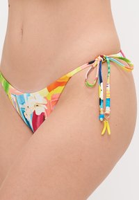 Spalvingos bikini kelnės su gėlėta raštu. Savybės: reguliuojamos šnerves su dekoratyvinėmis karoliukais ir maža geltona žavesiu. Pagamintos iš lygaus audinio.