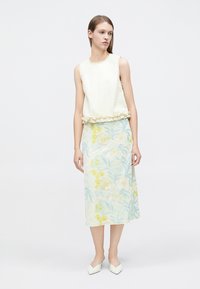 Haut blanc sans manches avec des accents de fleurs texturées, associé à une longue jupe claire à motifs floraux. Chaussures blanches simples à bout pointu.