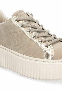 Baskets en daim beige avec un panneau à œillets métalliques dorés, des lacets ronds beiges, un logo embossé sur le côté et une épaisse semelle plateforme blanche rainurée.