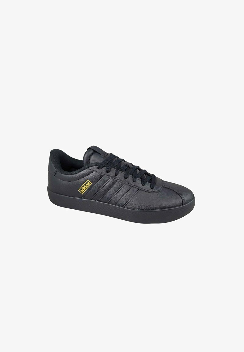 Chaussure de sport en cuir noir avec une semelle en caoutchouc, dotée de trois rayures surélevées, d'un embout rond et de lacets noirs. Petit logo jaune sur le côté.