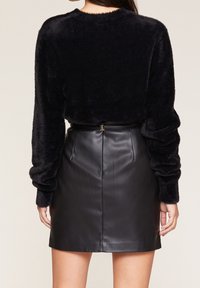 Svart lurvig tröja med långa, lätt samlade ärmar, kombinerad med en figursydd svart läderminikjol med söm baktill och bältesdetalj.