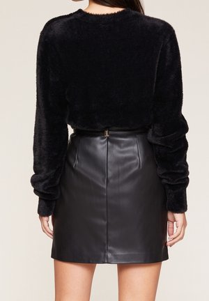 Czarny, puszysty sweter z długimi, lekko marszczonymi rękawami, zestawiony z dopasowaną czarną skórzaną mini spódnicą z tylnym szwem i detalem w postaci paska.