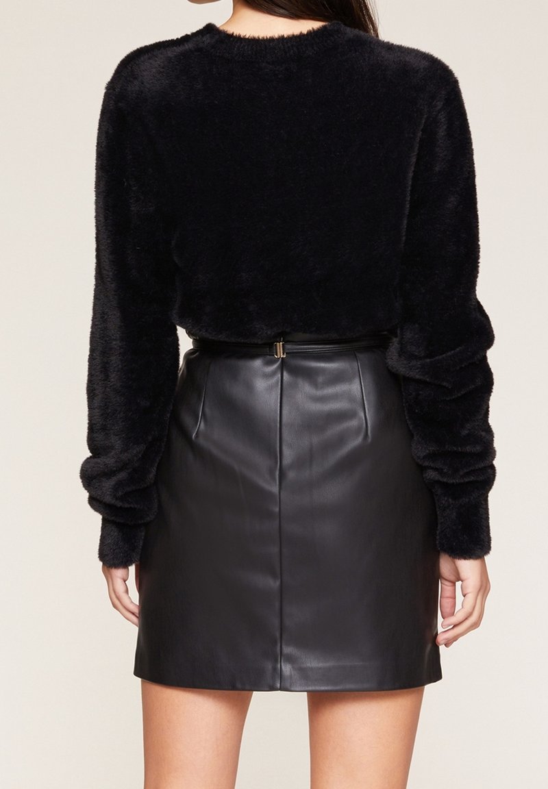 Svart lurvig tröja med långa, lätt samlade ärmar, kombinerad med en figursydd svart läderminikjol med söm baktill och bältesdetalj.