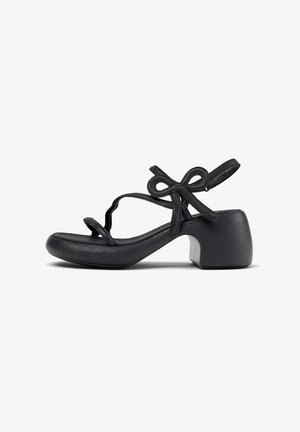 Sort hælet sandal med buet remdesign og dekorativ sløjfedetalje, med lav blokhæl og ankelrem.