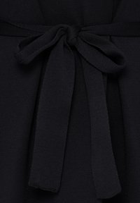 Ceinture en tissu noir nouée en nœud autour d'un vêtement noir texturé.