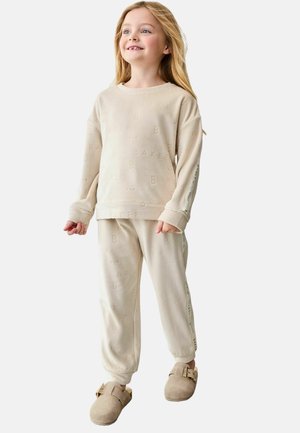 Beige bomulds loungewear sæt med struktureret "BAKER" print, lange ærmer, bukser med elastisk talje og beige slip-on sko.