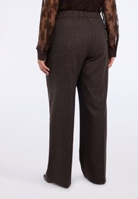 Brązowe spodnie z szerokimi nogawkami o delikatnym wzorze w prążki i złotymi drobinkami, z elastycznym paskiem w talii dla komfortu. Gładka faktura materiału.