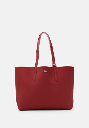 Sac cabas en cuir rouge avec deux longues anses et un petit logo crocodile argenté au centre devant sur fond blanc.