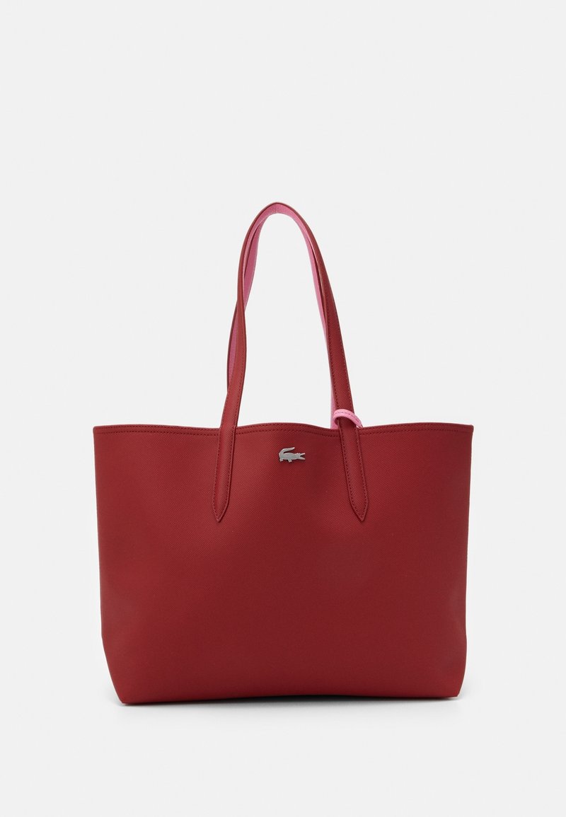 Sac cabas en cuir rouge avec deux longues anses et un petit logo crocodile argenté au centre devant sur fond blanc.