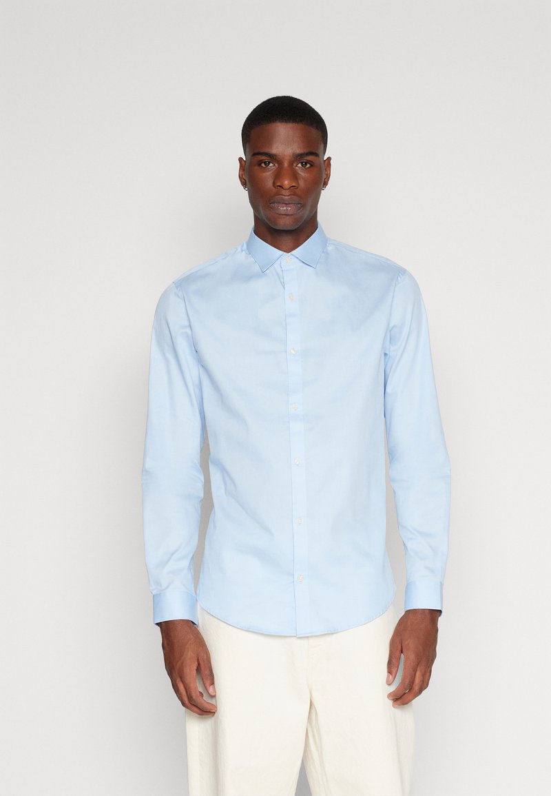 Camisa abotonada de manga larga, azul claro, confeccionada con una tela suave. Presenta un cuello clásico, cierre frontal de botones y una silueta ajustada.