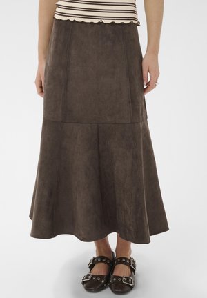 Femme portant une jupe midi en daim marron avec une taille ajustée et un ourlet évasé, associée à des chaussures noires à boucle et un haut rayé.
