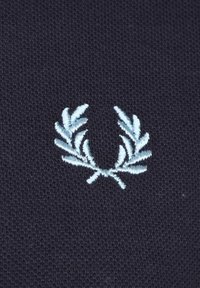 Tela de un azul marino oscuro con una textura entrelazada, con un logotipo de corona de laurel bordado en azul claro centrado en el material.