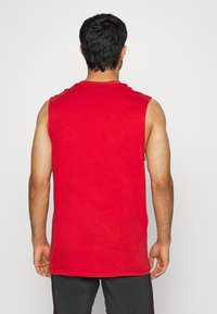 Czerwona koszulka bez rękawów wykonana z bawełny, z okrągłym dekoltem i prostym krojem. Widok z tyłu pokazuje gładką teksturę i minimalne detale.
