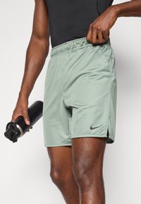 Pantalones cortos deportivos de color verde claro con cintura elástica, aberturas laterales para mayor movilidad y un pequeño logo negro de Nike en la parte inferior de la pierna.