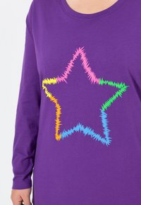 Violetti pitkähihaine paita, jossa etupuolella on värikäs sahalaitatähti-kuvio pinkissä, keltaisessa, oranssissa, vihreässä ja sinisessä.