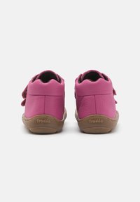 Roze leren schoenen met een gestructureerde afwerking, voorzien van een bruine rubberen zool en een verstelbare klittenbandsluiting aan de zijkant.