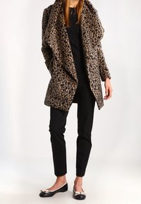 Abrigo de tela suave con estampado de leopardo y grandes solapas. Combinado con una blusa negra y pantalones negros, y bailarinas negras con un detalle de lazo.