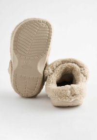 Zapatillas de casa beige y esponjosas con una suela de goma texturizada; forro suave y peludo alrededor de la apertura; diseño sin cordones para mayor comodidad y facilidad.