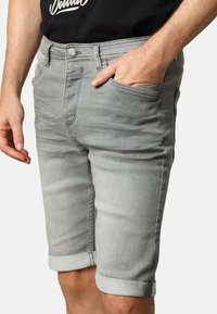 Shorts en denim gris clair avec un design ajusté, des ourlets retroussés et des poches avant. Dotés d'un bouton en métal et d'une texture discrète.