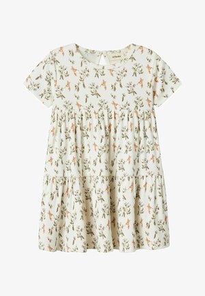 Kratkoročna, svetla obleka s cvetličnim vzorcem, večplastno oblikovana in z odprtinami na hrbtni strani. Narejena je iz navijalne tkanine, primerna za toplo vreme.