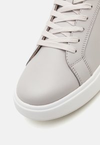 Helle graue Schuhe aus glattem Lederobermaterial, mit Schnürverschluss und weißer Gummisohle. Mit einem gesteppten Akzent entlang der Seite.