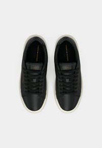 Pantofi sport negri din piele cu șireturi plate, talpă albă din cauciuc și detalii aurii cu logo pe limbă și lateral, având o textură netedă.