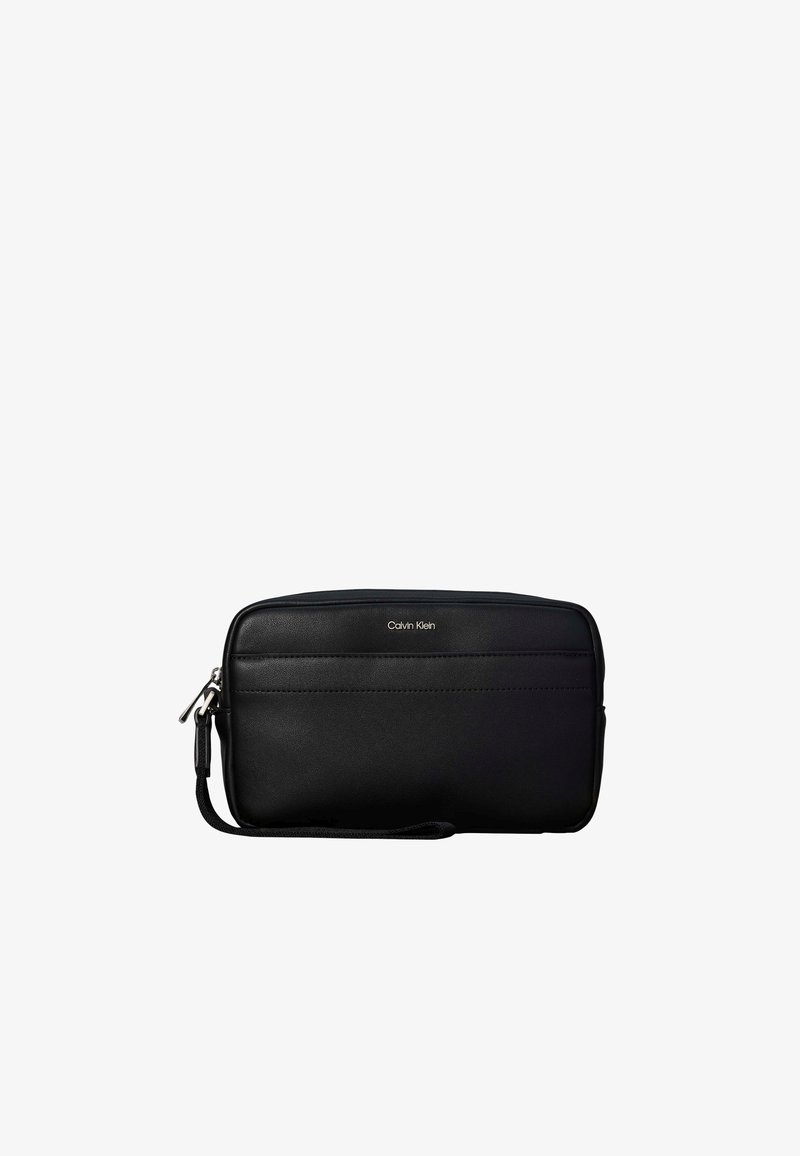 Μαύρο wristlet τσάντα Calvin Klein με μπροστινή τσέπη με φερμουάρ και μικρό λουράκι στην αριστερή πλευρά, πάνω σε λευκό φόντο.