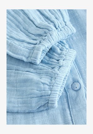 Lichtblauwe, gestructureerde stof met geplooide manchetten en een knoopdetail. Zachte, gekreukte uitstraling met een subtiel patroon door het hele materiaal.