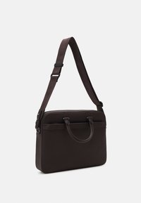 Musta ruskea nahkalaukku kannettavalle tietokoneelle, jossa on säädettävä olkahihna ja kaksi pientä kahvaa, esitettynä vaaleataustaista taustaa vasten.