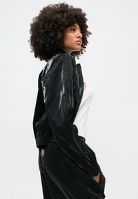 Μαύρο, γυαλιστερό μπουφάν bomber με μπροστινό φερμουάρ, ραμμένες μανσέτες και ζώνη μέσης. Διαθέτει κάθετες ρίγες κατά μήκος των μανικιών.