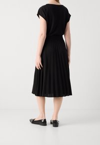 Mustat halkiot juhlapuvut lyhyillä hihoilla, kapea vyötärö ja sileä kangas. Yhdistetty mustiin ballerina-kenkiin, korostaen minimalistista muotoilua.