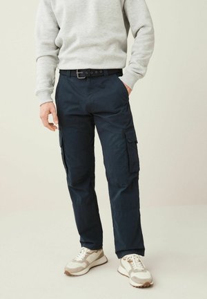 Marina cargobyxor gjorda av lättviktigt tyg, med flera fickor, en smal passform och ett bälte med ett silverfärgat spänne. Bärs tillsammans med en grå sweatshirt.