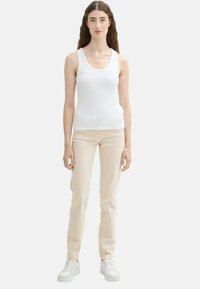 Biały podkoszulek z żebrowanej tkaniny w połączeniu z dopasowanymi beżowymi spodniami i białymi trampkami, prezentujący smukłą sylwetkę i minimalistyczny design.
