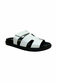 Chanclas blancas con suela negra, que presentan dos correas anchas con diseños troquelados y cierre ajustable de velcro. Textura de cuero suave.