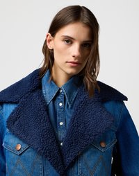 Spijkerjack met een donkerblauwe, gestructureerde, schapenwollen kraag. Kenmerken zijn onder andere voorzakken, koperen hardware en contrasterende blauwe stof.