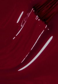 Deep red nail polish with a glossy finish, displaying a smooth texture, and a brush resting against the surface, capturing a shiny reflection.