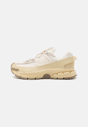 Baskets basses beige et crème avec semelle épaisse, semelle intermédiaire texturée, logo Nike « swoosh » et fermeture à lacets sur fond uni.