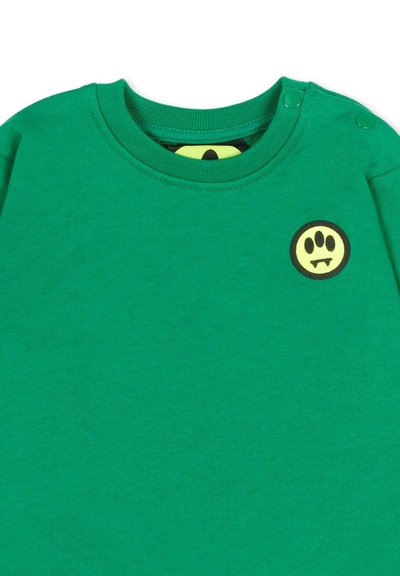 Felpa verde per bambino piccolo con scollo rotondo, bottoni a pressione sulla spalla e una piccola toppa con il volto di un mostro cartoon giallo e nero sul petto.