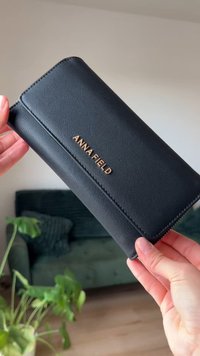 Černá peněženka ze syntetické kůže s hladkou texturou, s zlatým logem "ANNA FIELD" a zipovým uzávěrem.