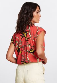 Blusa roja floral de mangas cortas, con patrones en verde y negro. La tela parece ligera y tiene una textura suave.