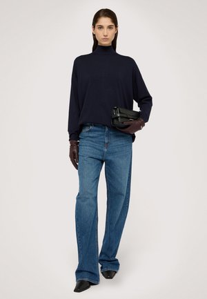 Marineblauer Strickrollkragenpullover, lockere Passform; blaue ausgestellte Jeans; dunkelbraune Lederhandschuhe; schwarze Handtasche; spitze schwarze Schuhe; minimalistisches Design.