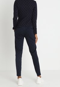 Marinblus med prickigt mönster och långa ärmar, tillsammans med matchande byxor. Mjuk tyg med en jämn yta, avslutat med vita skor.