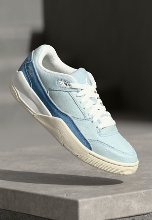 Lyseblå og hvide sneakers med hvide snørebånd og tekstureret sål, svævende over en betonoverflade i blødt lys.