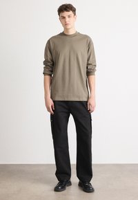 Chemise beige à manches longues avec un col ras du cou, associée à un pantalon cargo noir doté de poches latérales et d'une coupe droite. Porté avec des chaussures noires.