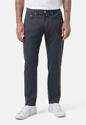 Grey cotton trousers with a slim fit, five-pocket design, and contrast stitching. Paired with white sneakers.